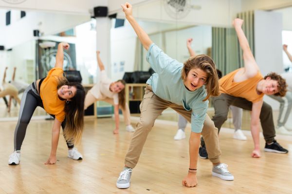 Jugendliche machen gemeinsam Tanzübungen in einer Sporthalle und bewegen sich synchron in der Gruppe.